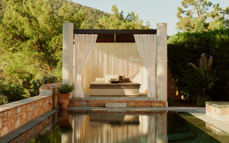 Wooden pavilion with seating area reflected in still water at Amanruya, surrounded by lush greenery.