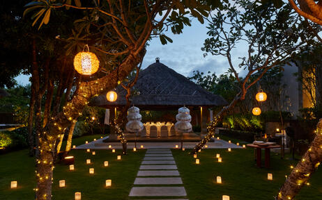 Illuminated pathway lined with lanterns leading to Aman Villas at Nusa Dua at dusk, with lush tropical grounds.