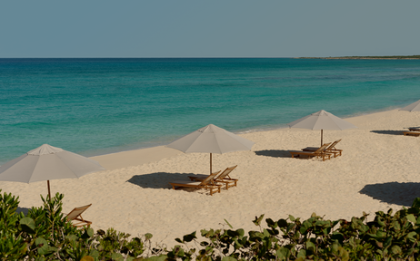 Soft sandy beach at Amanyara with turquoise waters and scattered sun shelters.