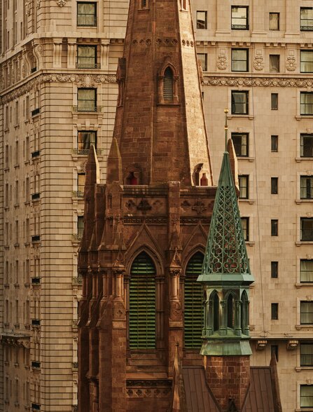 Historic copper-roofed church building on Fifth Avenue, surrounded by tall stone buildings in New York.