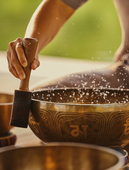Hands striking a singing bowl during sound healing meditation at Amanoi spa and wellness centre.