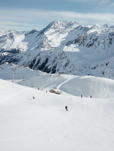 Skieurs sur les pistes enneigées d'Aman Le Mélézin, avec montagnes enneigées en arrière-plan.
