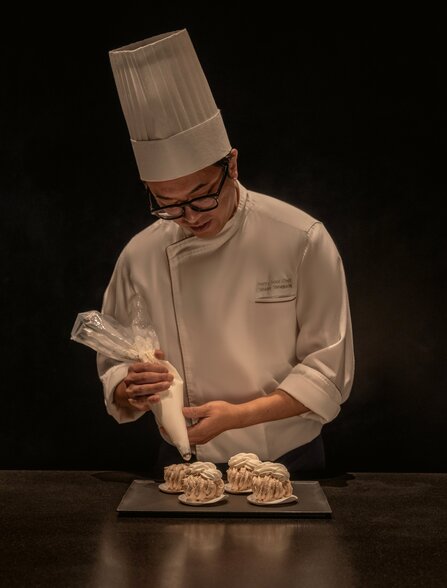 Chef at Aman Tokyo's La Pâtisserie plating a delicate dessert with focused precision.