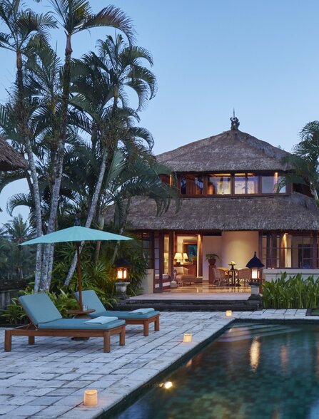 Asmara Pool Villa's swimming pool illuminated at night, with the villa's warm interiors glowing beyond at Amandari, Bali.