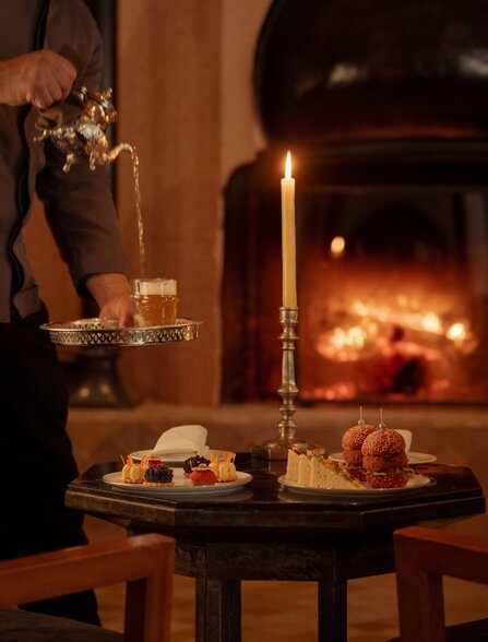 Bar at Amanjena with fireplace glow illuminating drinks and snacks on a table.