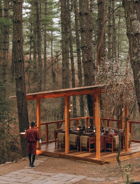 Wooden dining structure with glass panels set amongst tall forest trees at Amankora, Thimphu.