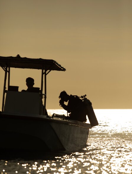 Silhouetted divers preparing equipment aboard the Aman XVII boat at Amanwana, Indonesia.