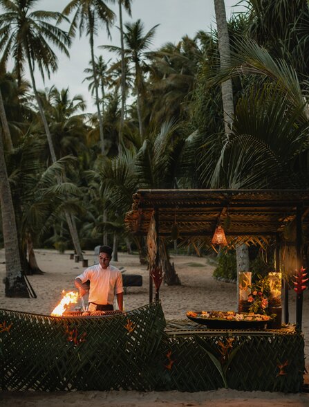 Candlelit beachside dining setup at Amanwella with palm trees and ocean views at dusk.