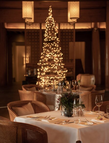 Illuminated Christmas tree decorated with warm lights in Amandayan's dining room, set for an evening celebration.