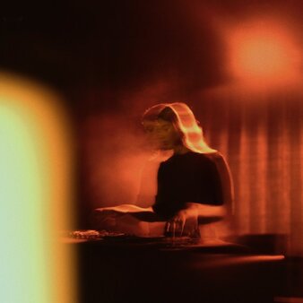 DJ performing at The Jazz Club, Aman New York, with warm amber lighting and musical equipment.