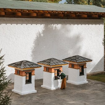 Entrance to Amankora's Thimphu Lodge, featuring traditional wooden shelter structures with tiered roofs on a stone courtyard.
