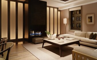 Evening view of a corner suite living room at Aman New York, featuring a fireplace, neutral tones, and contemporary furnishings.