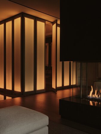 Grand Suite bedroom with illuminated wooden partition screen and fireplace at Aman New York.