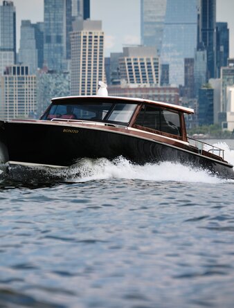 Sleek black speedboat cutting through Hudson River waters with Manhattan skyline behind, Aman New York.