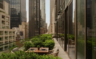 Verdant terrace with wooden bench overlooking Manhattan skyscrapers at Aman New York.