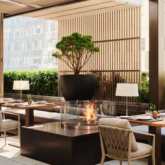 Arva Garden Terrace dining room at Aman New York, with tables, chairs, and a sculptural tree centrepiece.