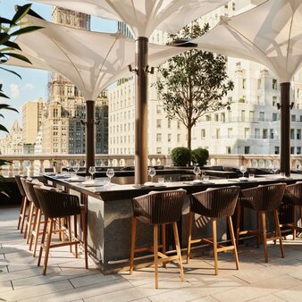 Garden terrace bar at Aman New York with wooden seating and city views.