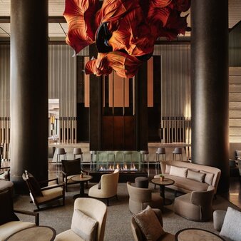Aman New York's lounge interior with soaring columns, contemporary seating arrangements, and a striking amber-toned sculptural installation overhead.
