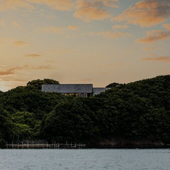 Amanemu's modern architecture positioned on a forested hillside at sunset, overlooking calm waters.