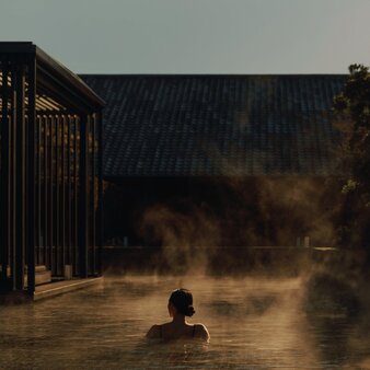 Guest bathing in steaming onsen at dusk, Amanemu.