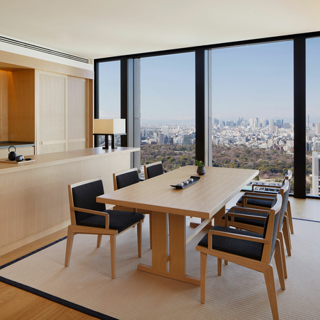 Modern workspace at Aman Tokyo with floor-to-ceiling windows overlooking the city skyline, wooden dining table, and contemporary chairs.
