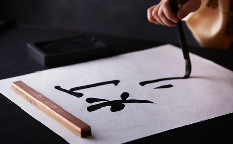 Hand holding brush, painting brushstrokes on paper at Aman Tokyo.