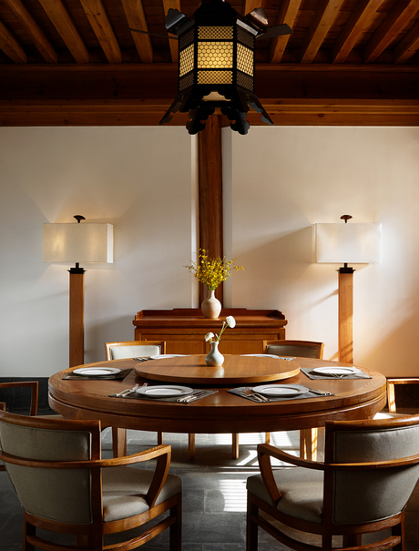 Wooden dining table beneath a brass pendant light at Amandayan, with exposed beam ceiling and upholstered chairs.