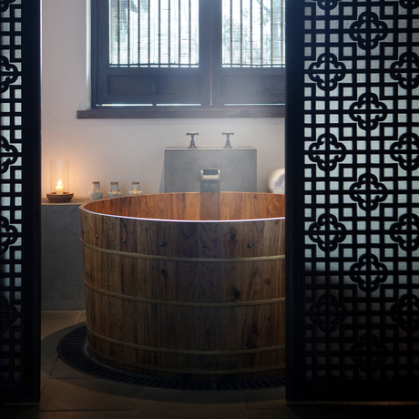 Wooden soaking tub with candlelit ambiance at Amanfayun, framed by geometric screen panels.