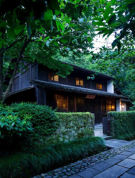 Amanfayun pavilion nestled amongst lush greenery with warm interior lighting at dusk.