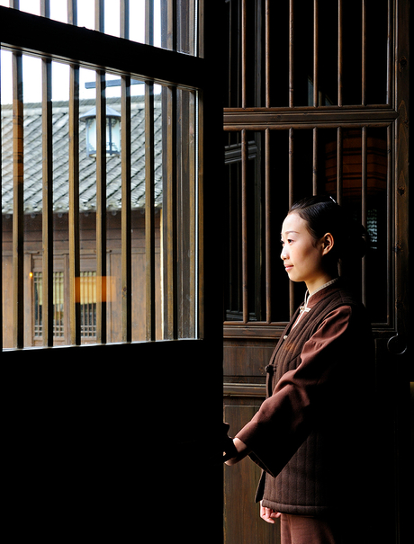 Woman standing in traditional wooden doorway at Amanfayun, filtered light creating geometric shadows.