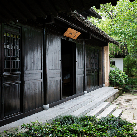 Black wooden pavilion with double doors at Amanfayun, framed by lush greenery.