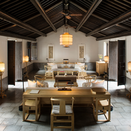 Gallery space at Amanfayun with wooden furniture and neutral tones, featuring a central table arrangement and pendant lighting.