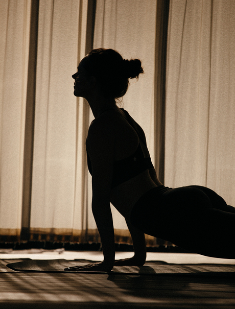 Silhouetted figure in downward dog yoga pose at Amanyara, with sheer curtains and geometric shadow play.
