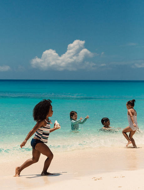 Children playing in turquoise waters at Amanyara's beach beneath clear skies.