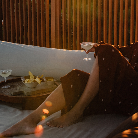 Guest relaxing with a cocktail on a lounger at Amanyara, with warm light and wooden wall panels.