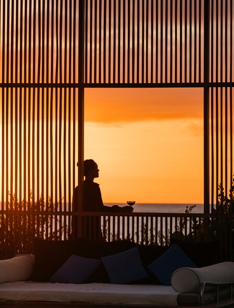 Silhouetted figure on a wooden deck at sunset, framed by vertical timber screens at Amanyara.