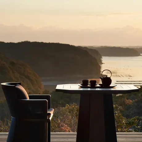 Table and chairs on a terrace overlooking coastal landscape at dusk, Amanemu resort.