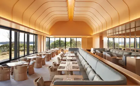 Salle à manger spacieuse au plafond voûté en bois clair, tables dressées et vues panoramiques à Amanemu.