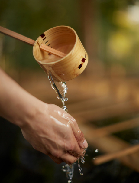 Water pours from a wooden dipper into an open hand at Amanemu resort.