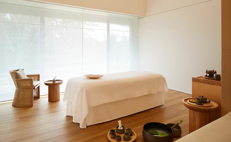 Serene spa treatment room at Amanemu resort with a draped massage bed and natural light from floor-to-ceiling windows.