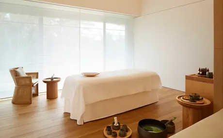 Spa treatment room at Amanemu resort with a draped massage table, wooden vessels, and natural light from large windows.
