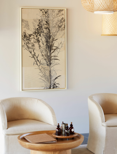 Cream curved chair with wooden side table holding spa bottles, botanical artwork above, Amanemu resort.