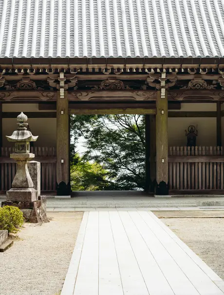 Wooden temple gateway with white-painted floor at Amanemu resort, framing a glimpse of gardens beyond.