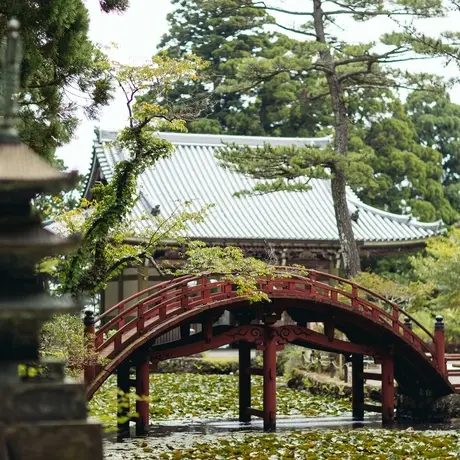 Arched wooden bridge at Amanemu resort, framed by lush green foliage.