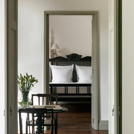 View through doorway to Amangalla bedroom with framed mirror and fresh flowers on side table.