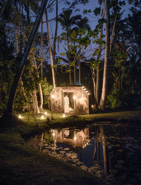 Amangalla pavilion illuminated at dusk, reflected in still water amongst towering palms.