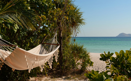 Hammock strung between palm trees overlooking turquoise waters at Amanpulo resort.