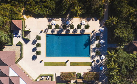 Aerial view of Amanpulo's swimming pool surrounded by sun loungers and lush tropical vegetation.