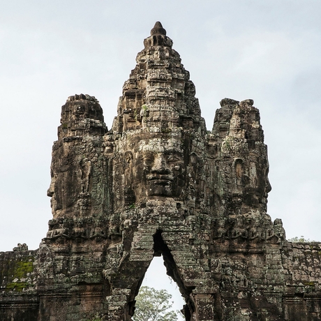 Stone temple tower at Amansara, Cambodia, with carved faces and archway entrance.