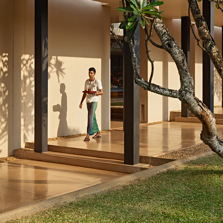 A guest stands in a villa's open-air pavilion at Amanwella, framed by timber columns and overlooking manicured gardens.
